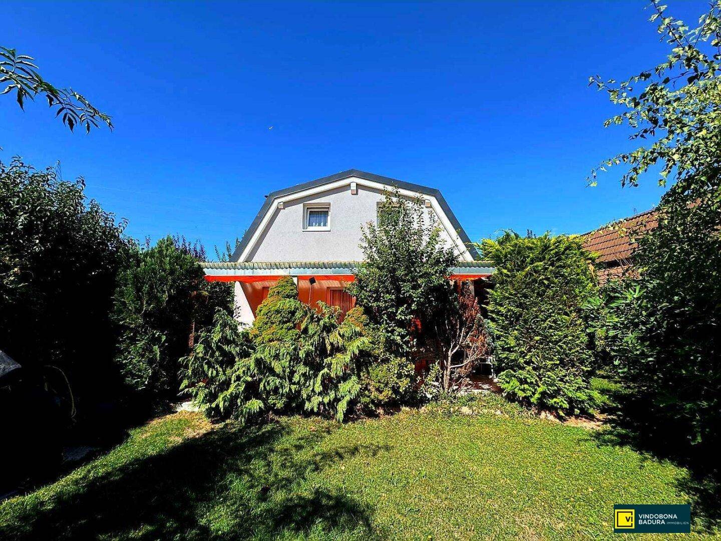 Rückansicht des Hauses mit einem überdachten Bereich und einem gepflegten Garten mit Rasen.
