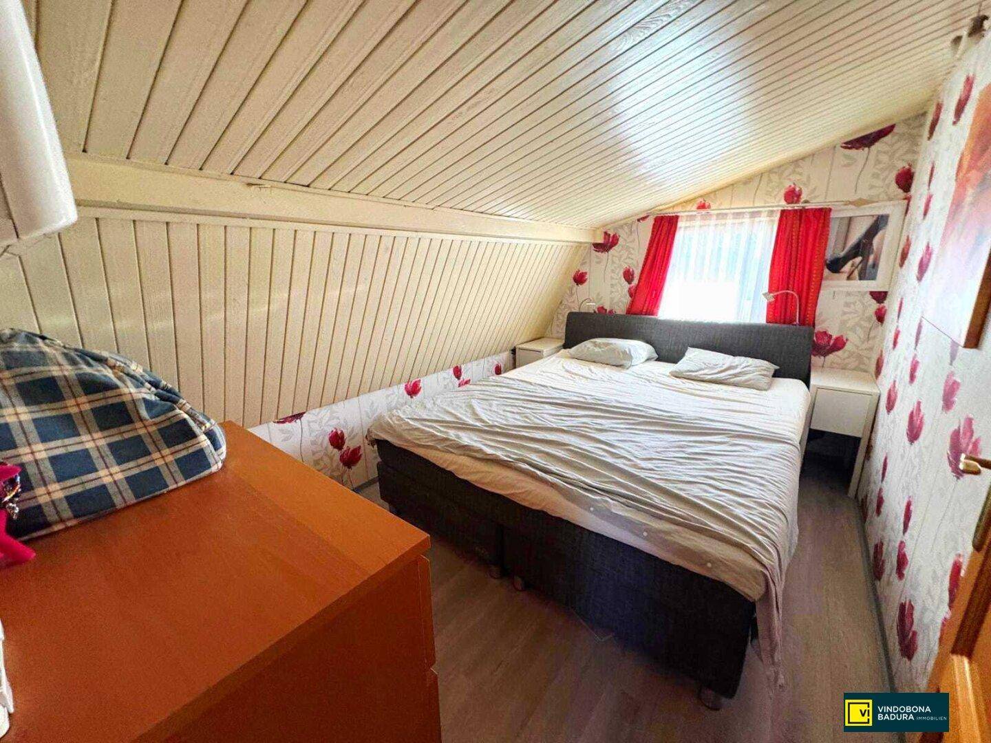 Schlafzimmer im Dachgeschoss mit Doppelbett, Dachschräge und floraler Tapete.