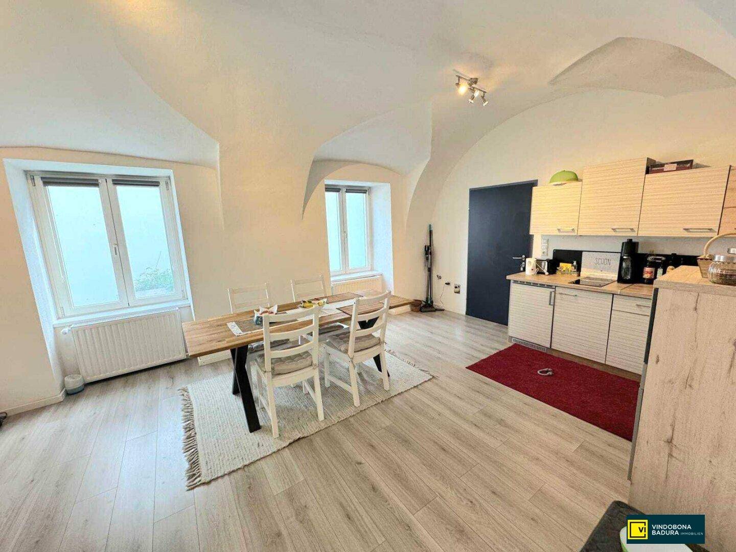 Essbereich mit Holztisch und Stühlen, kleiner Küche und beeindruckenden Gewölbedecken.
