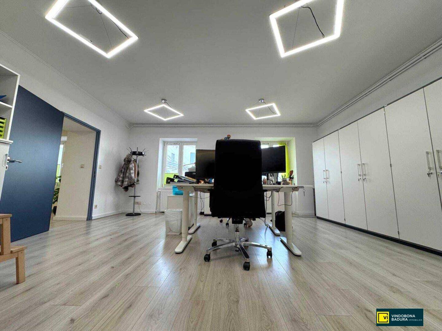 Helles Büro mit mehreren Arbeitsplätzen, integrierten Schränken und modernen Deckenleuchten.