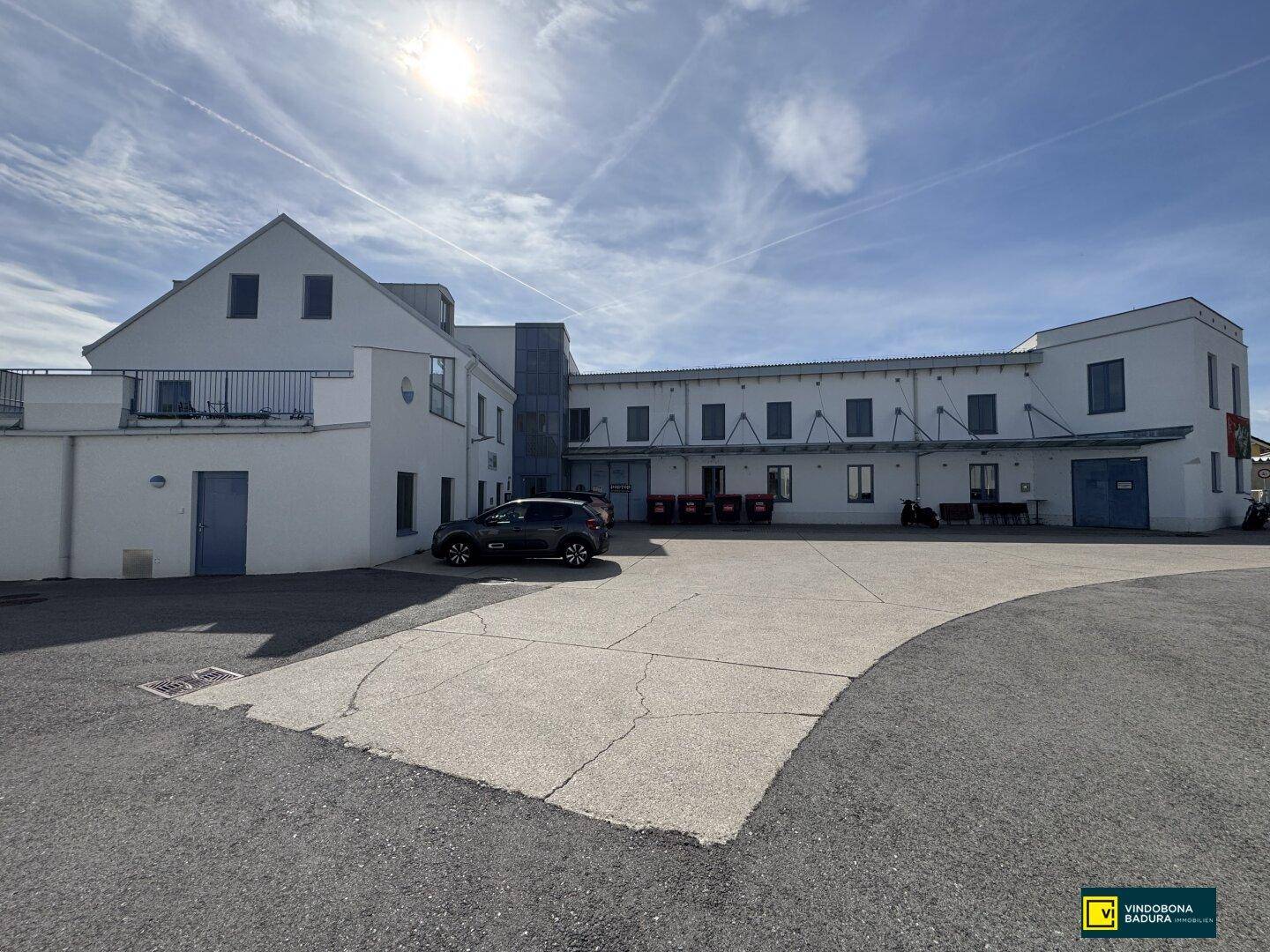 Außenansicht eines modernen Gebäudekomplexes mit großem Parkplatz unter blauem Himmel.