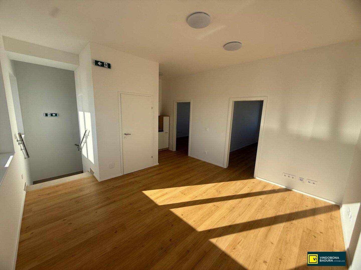 Helles Büro mit Holzfußboden und Zugang zu einem Flur, durchflutet von natürlichem Licht.