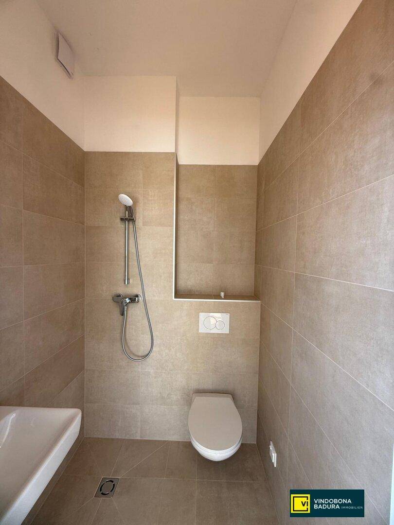 Modernes Badezimmer mit beigefarbenen Fliesen, wandhängendem WC und Duschbereich.