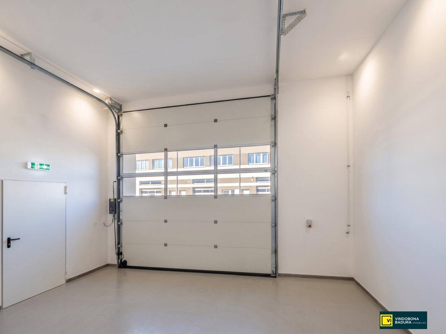 Geräumiger Gewerberaum mit großem Sektionaltor und Blick auf die gegenüberliegende Gebäudefassade.