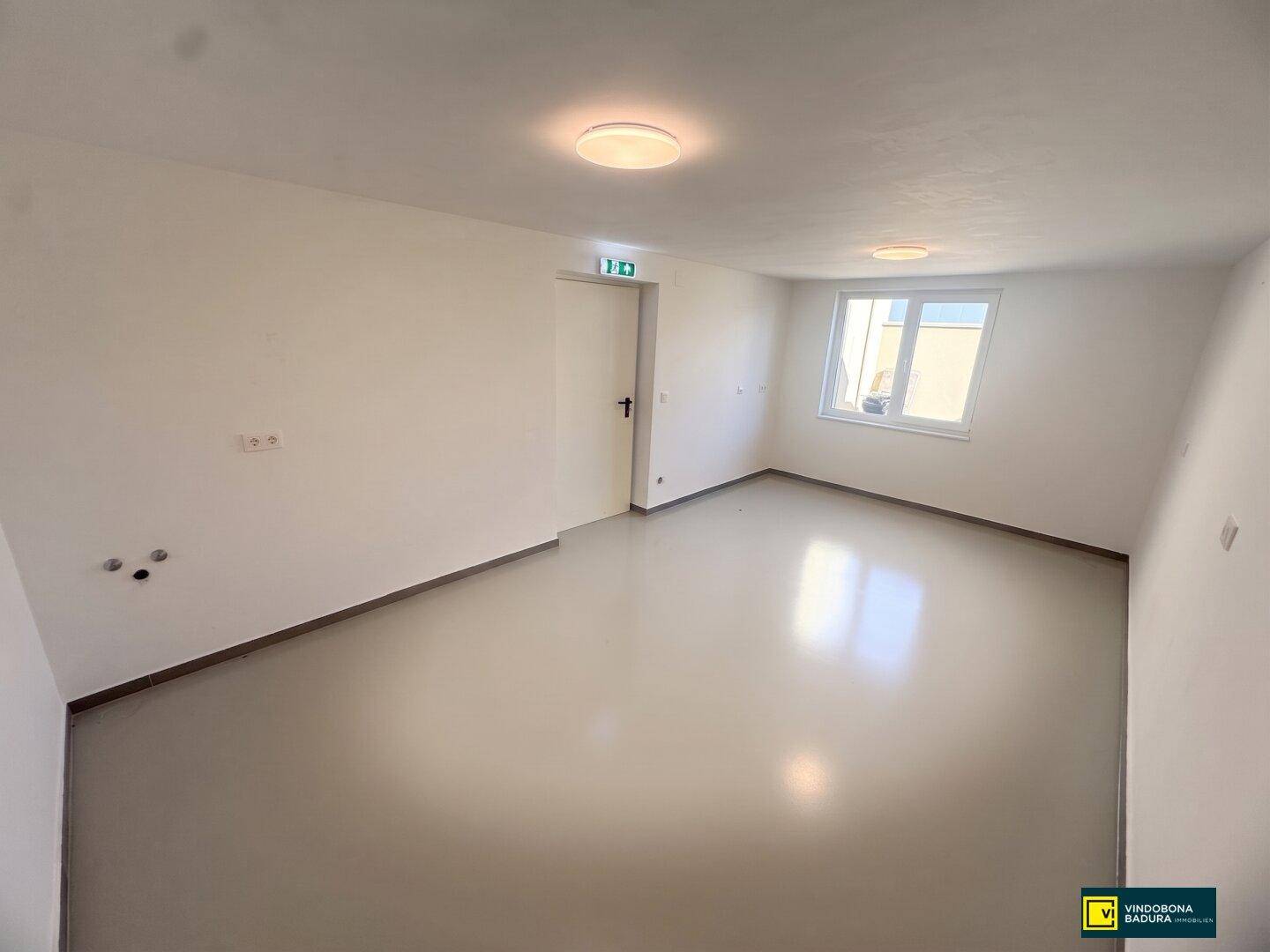 Heller, sauberer Raum mit glattem Boden, weißen Wänden und einem Fenster, ideal als Büro.