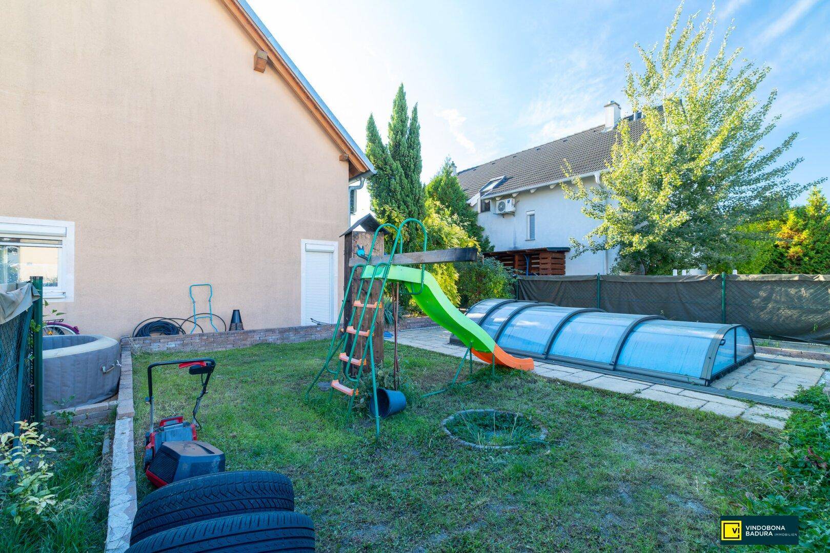 Gartenbereich mit Kinderrutsche, Rasen und überdachtem Pool, ideal für Familienaktivitäten im Freien.