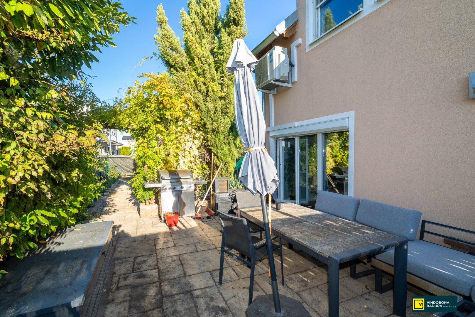 Sonniger Terrassenbereich mit Esstisch, Sonnenschirm und Grill, direkt am Haus gelegen.