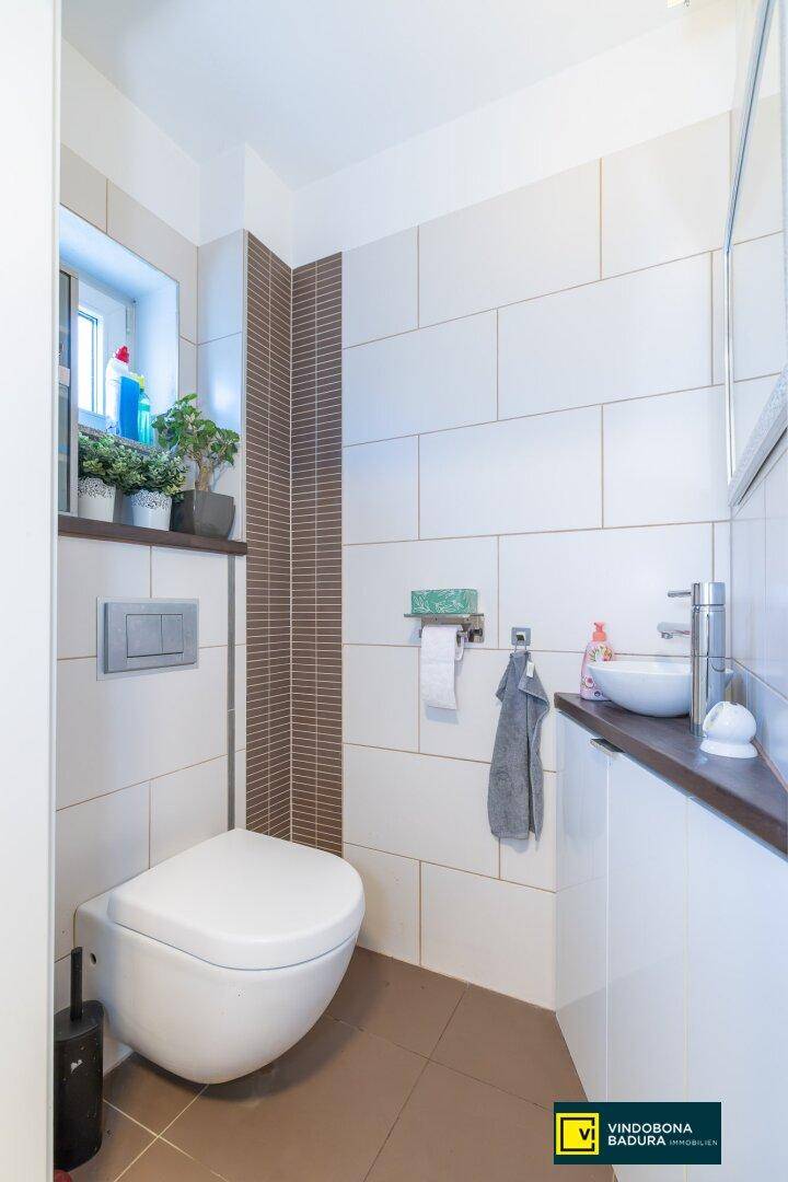 Modernes Gäste-WC mit Wand-WC, kleinem Waschbecken und Fenster für Tageslicht.