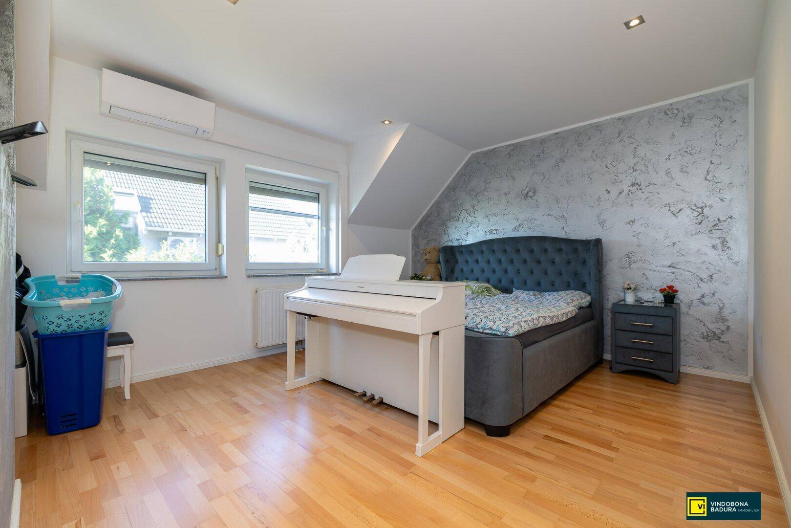 Gemütliches Schlafzimmer mit Holzboden, strukturierten Wänden und Dachschräge, inklusive Klimaanlage.