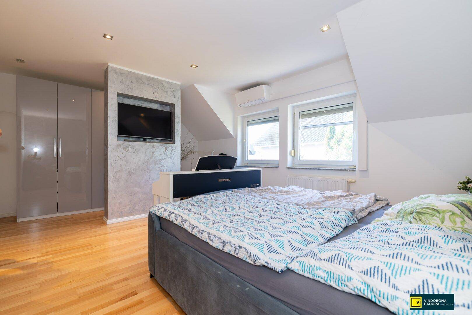 Modernes Schlafzimmer mit Holzboden, Einbauschränken und Dachschräge, ausgestattet mit Fernseher.