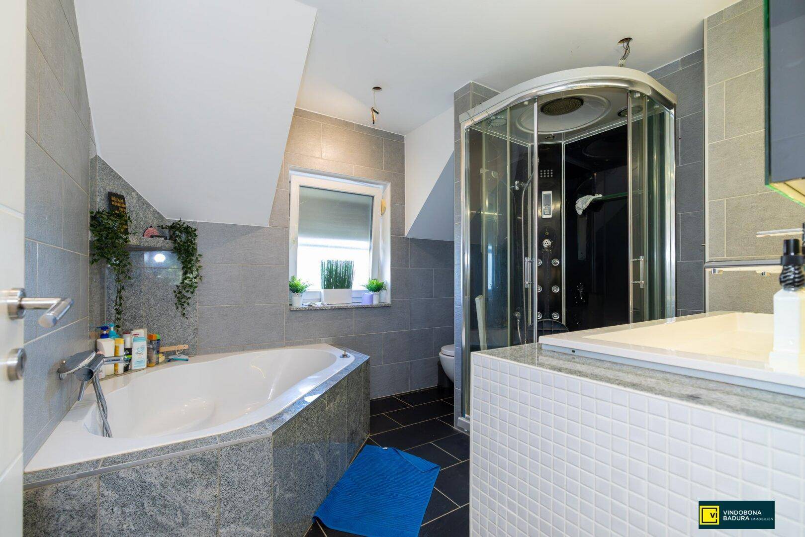 Modernes Badezimmer mit Eckbadewanne, Duschkabine und grauen Fliesen unter Dachschräge.