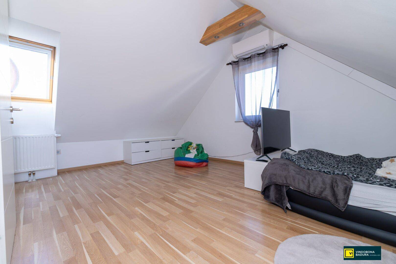 Helles Schlafzimmer im Dachgeschoss mit Holzboden, sichtbaren Holzbalken und Dachschräge.