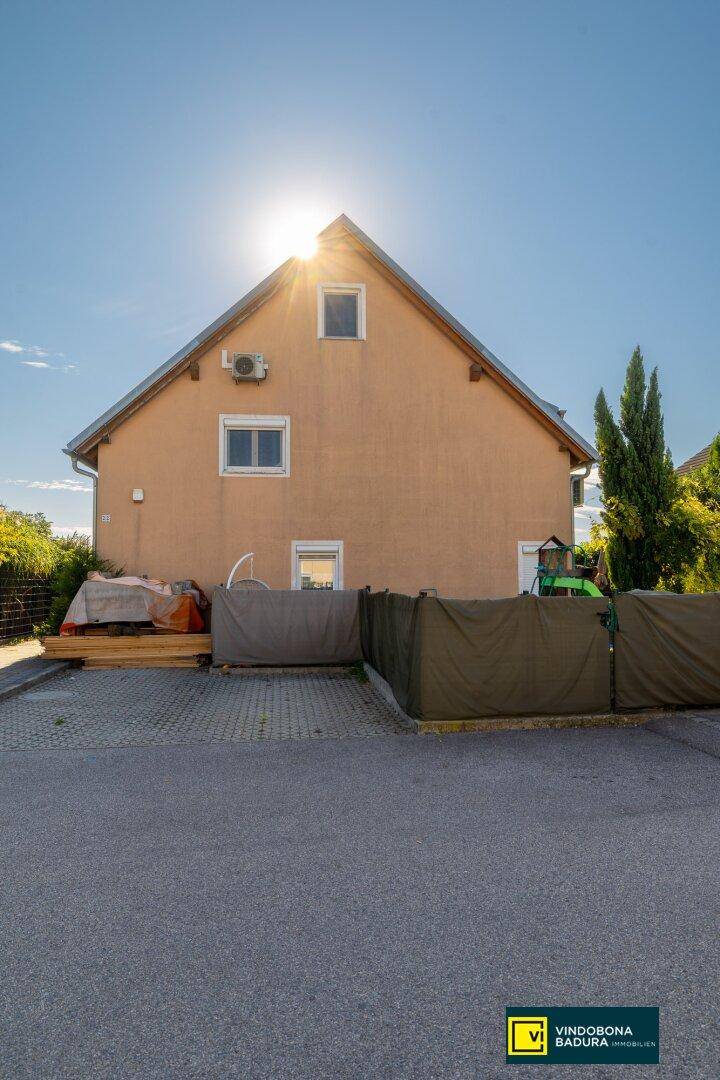 Rückansicht des Hauses mit Gartenbereich und sonnigem Himmel, umgeben von Grün.