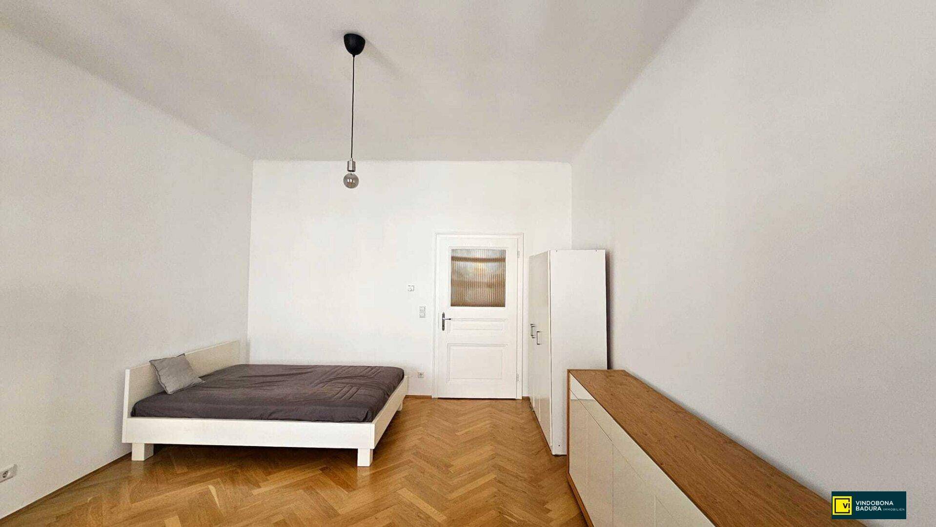 Schlafzimmer mit Fischgrätparkett, einem Bett und einem weißen Kleiderschrank.