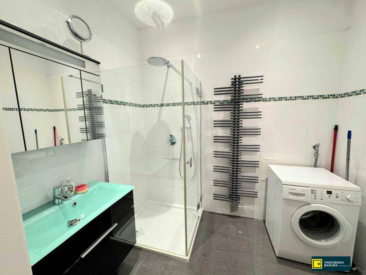 Modernes Badezimmer mit Duschkabine, Waschmaschine und beheiztem Handtuchhalter.
