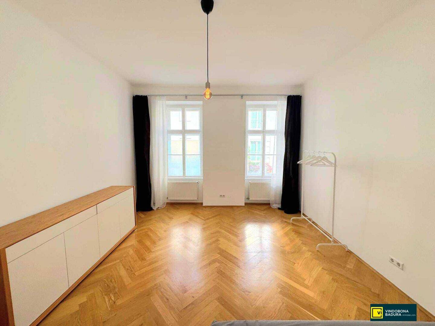 Helles Zimmer mit Fischgrätparkett, hohen Fenstern und einem modernen Sideboard.