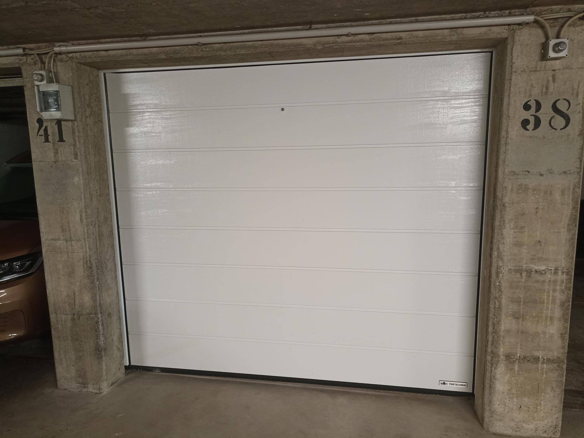 Geschlossenes weißes Garagentor einer privaten Garagenbox in einer Tiefgarage.