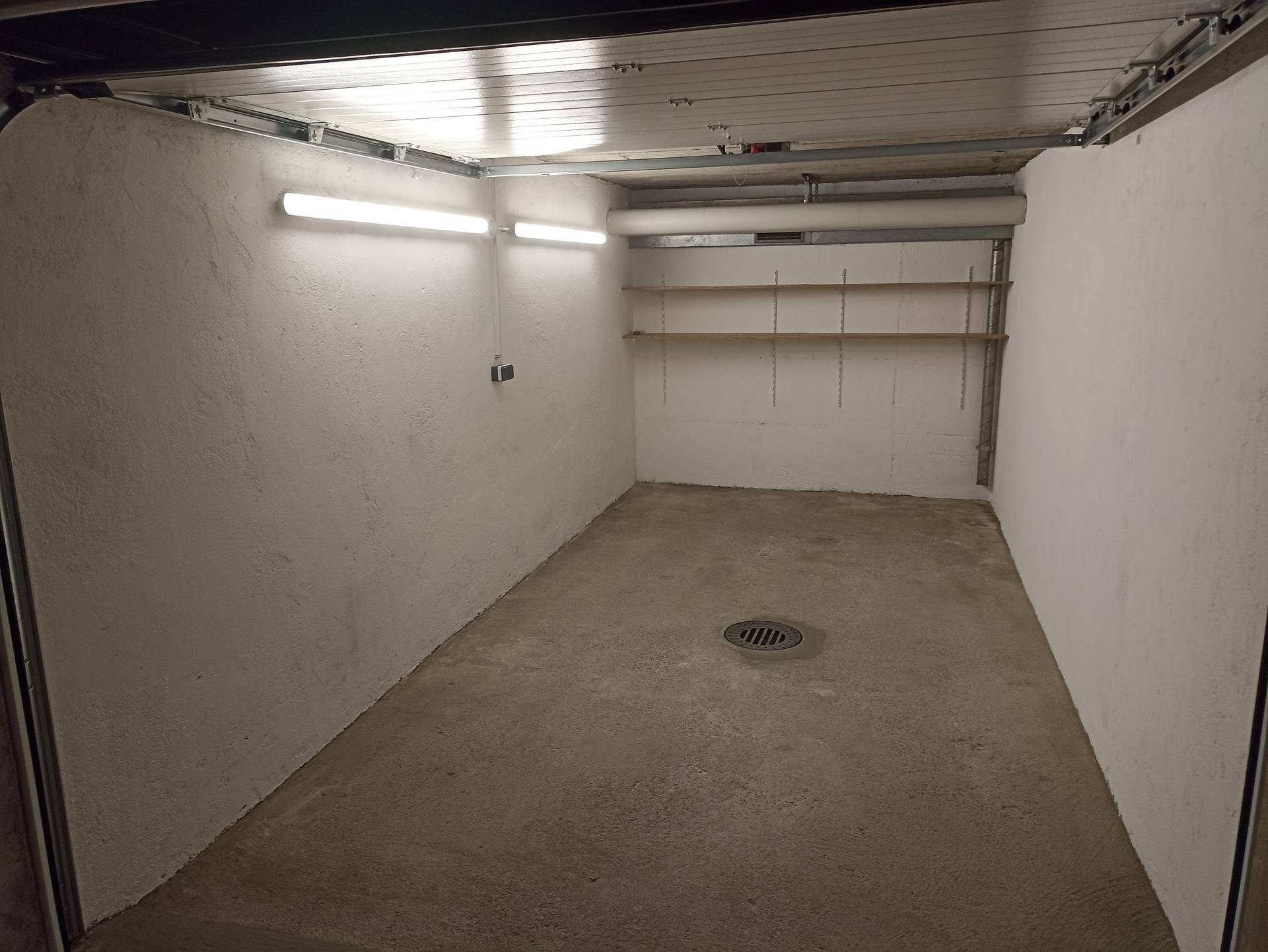 Geräumige Garagenbox mit Betonboden, Beleuchtung und Wandregalen, ideal für Fahrzeuge und Lagerung.