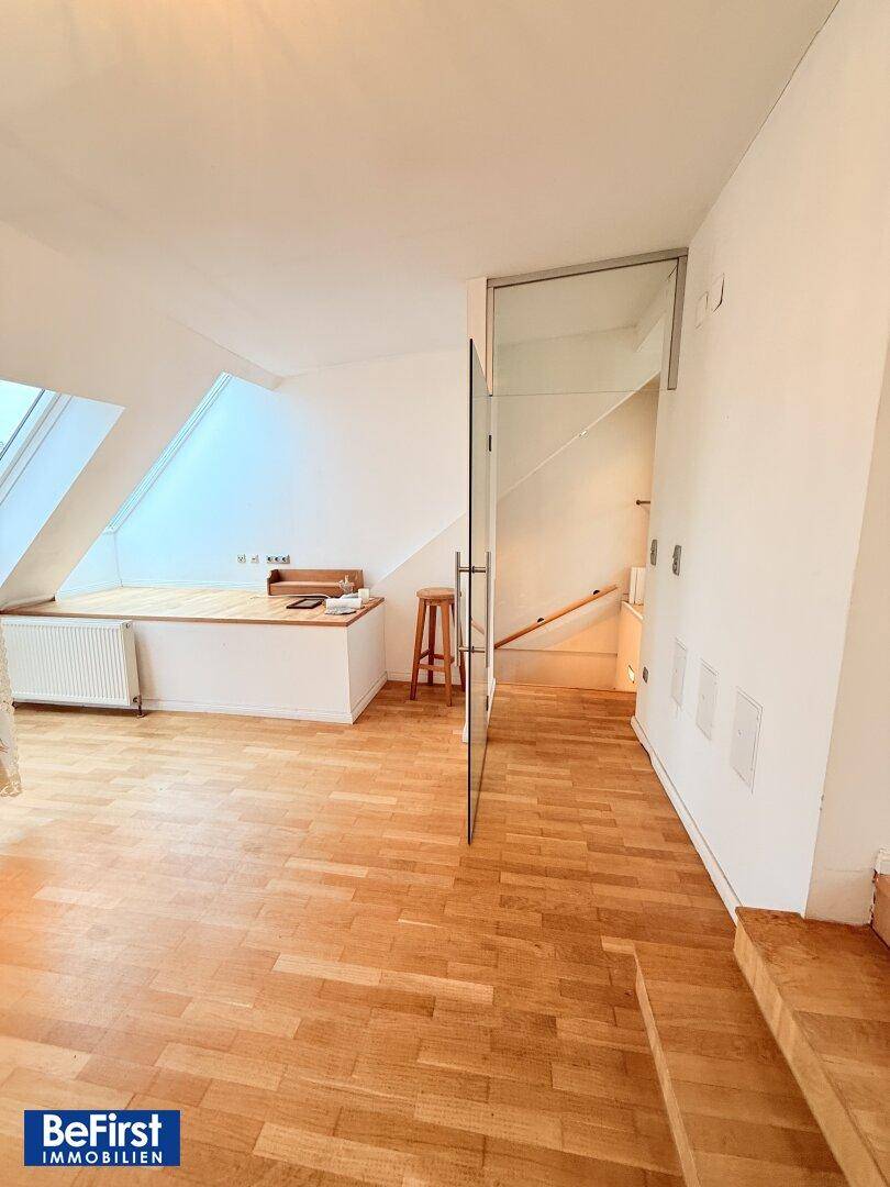 Heller Flur mit Holztreppe und Glasabtrennung, der zu den oberen Etagen führt.