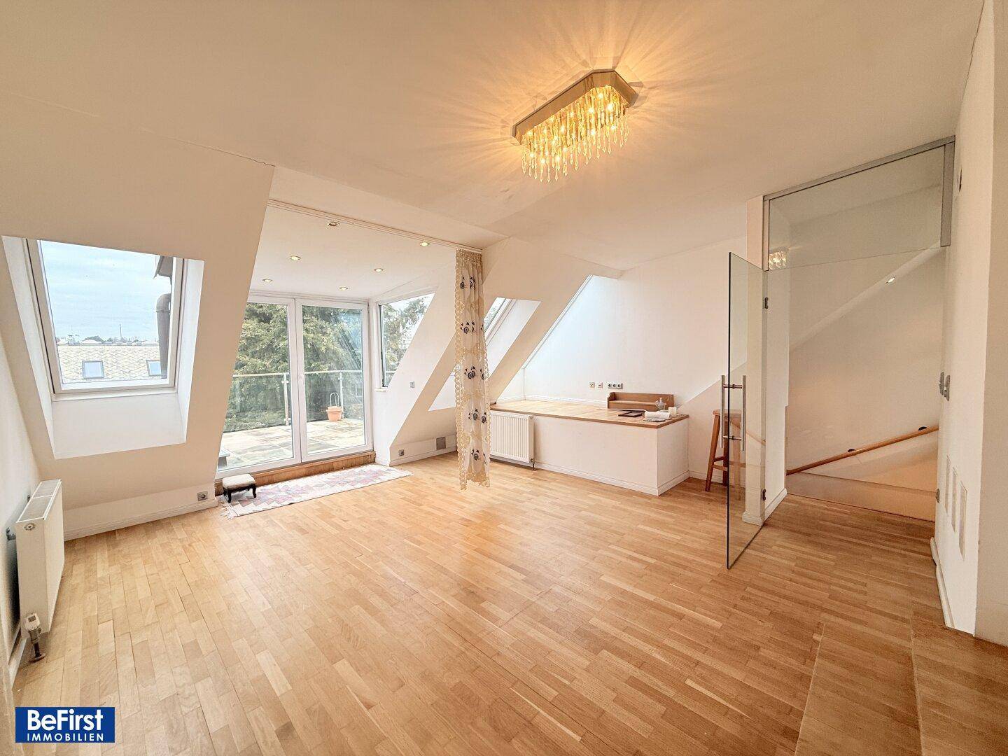 Heller Wohnraum im Dachgeschoss mit Parkettboden, Dachfenstern und Zugang zum Balkon.