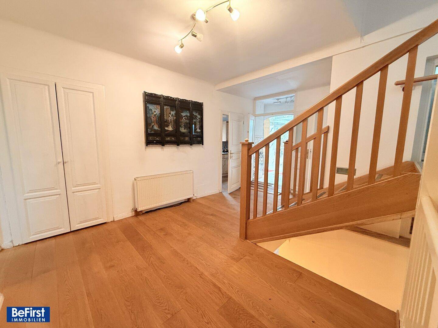 Heller Raum mit Holzparkett, eingebauten Schränken und einer Holztreppe.