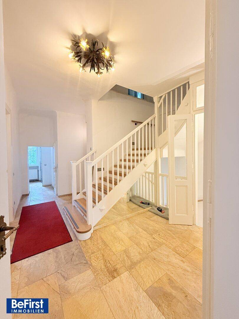 Geräumiger Eingangsbereich mit Marmorboden, weißer Holztreppe und dekorativem Kronleuchter.