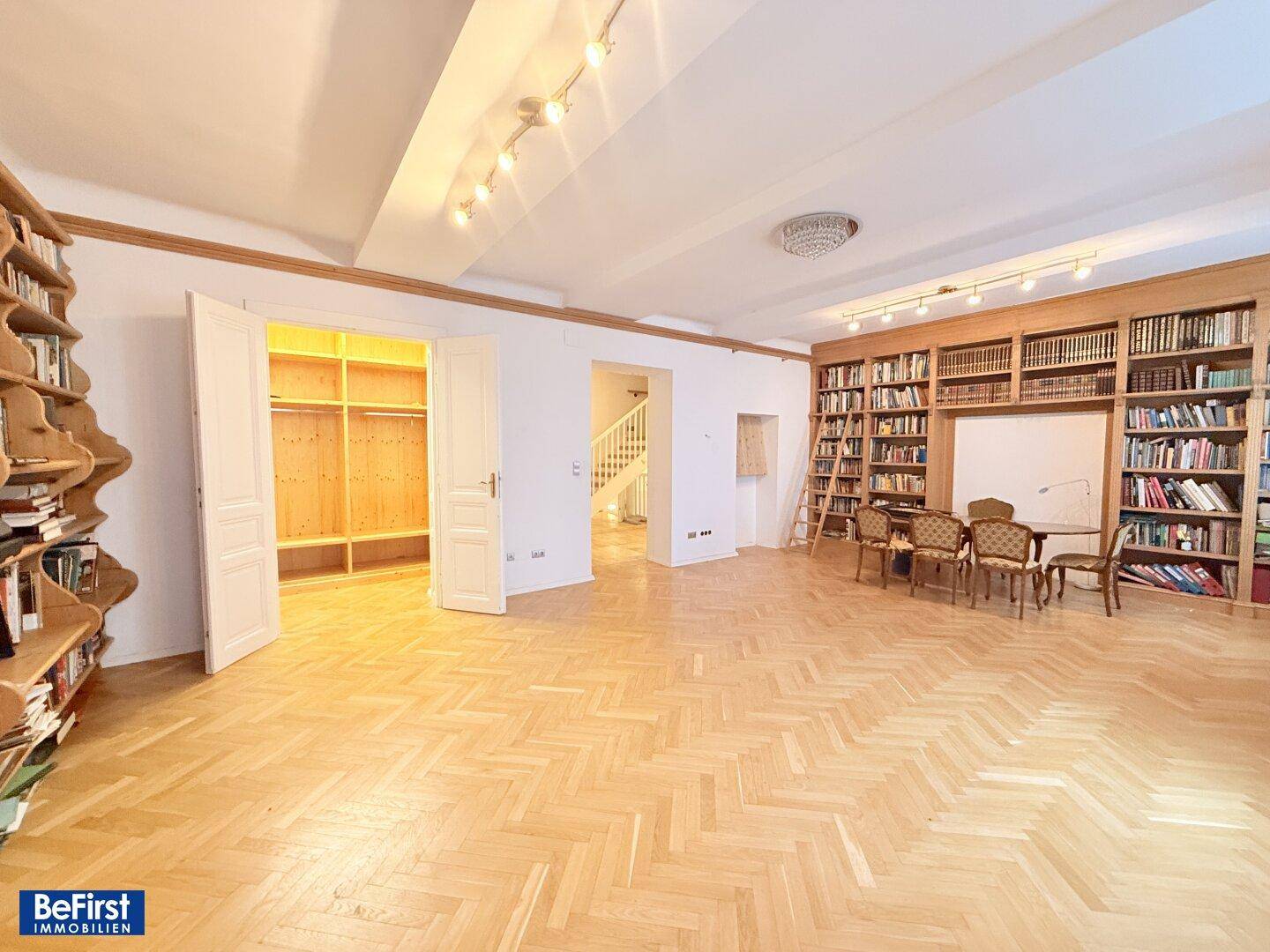 Großzügiger Raum mit Fischgrätparkett, hohen Decken und eingebauten Bücherregalen.