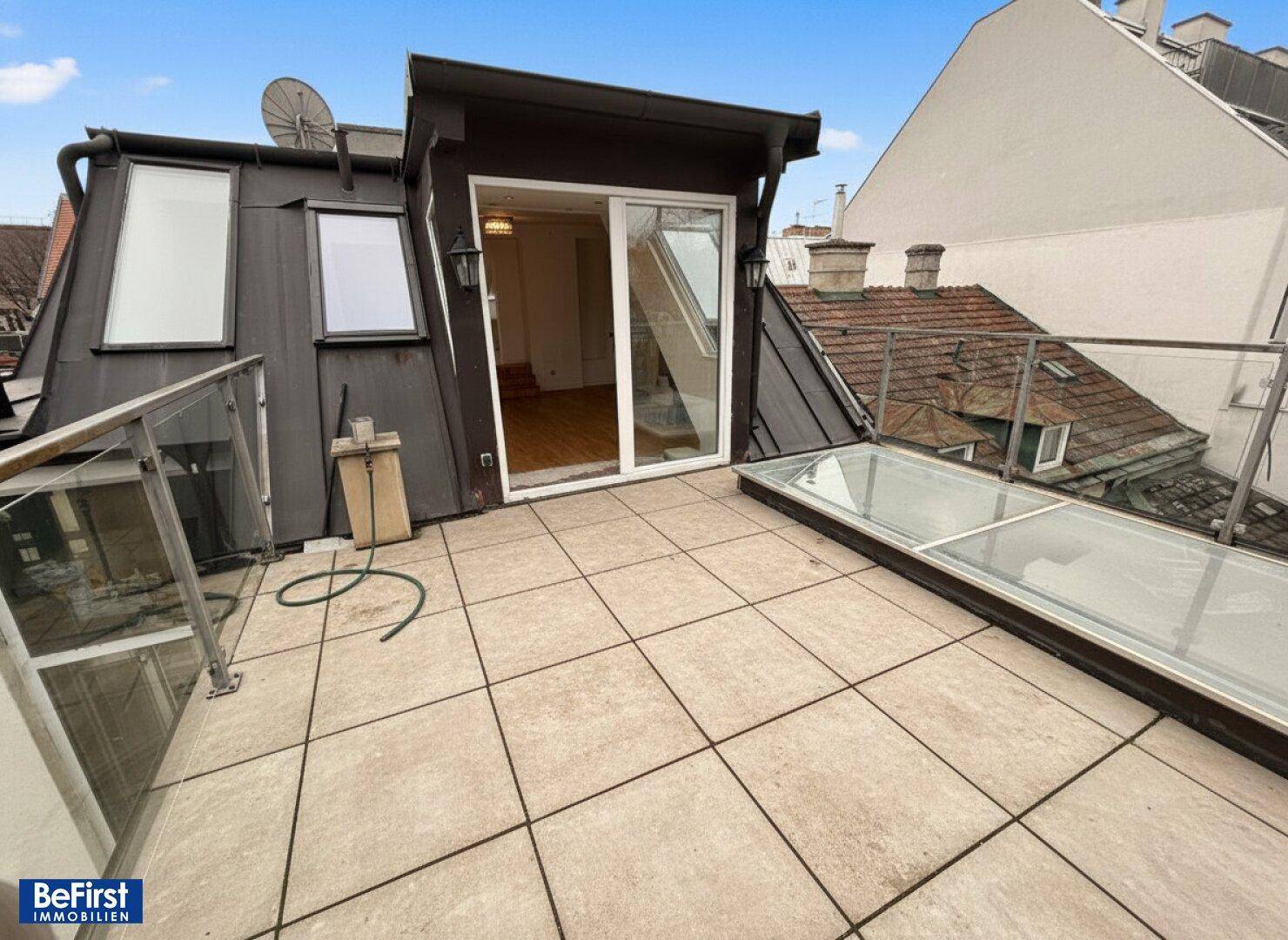 Dachterrasse mit Fliesenboden, Glasgeländer und Zugang zu einem Innenraum.