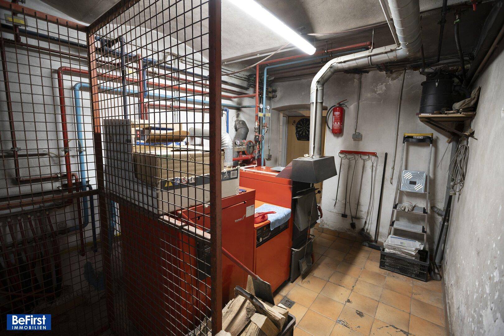 Heizungsraum mit Kessel, Rohren und Lagerfläche für Brennholz im Kellerbereich.