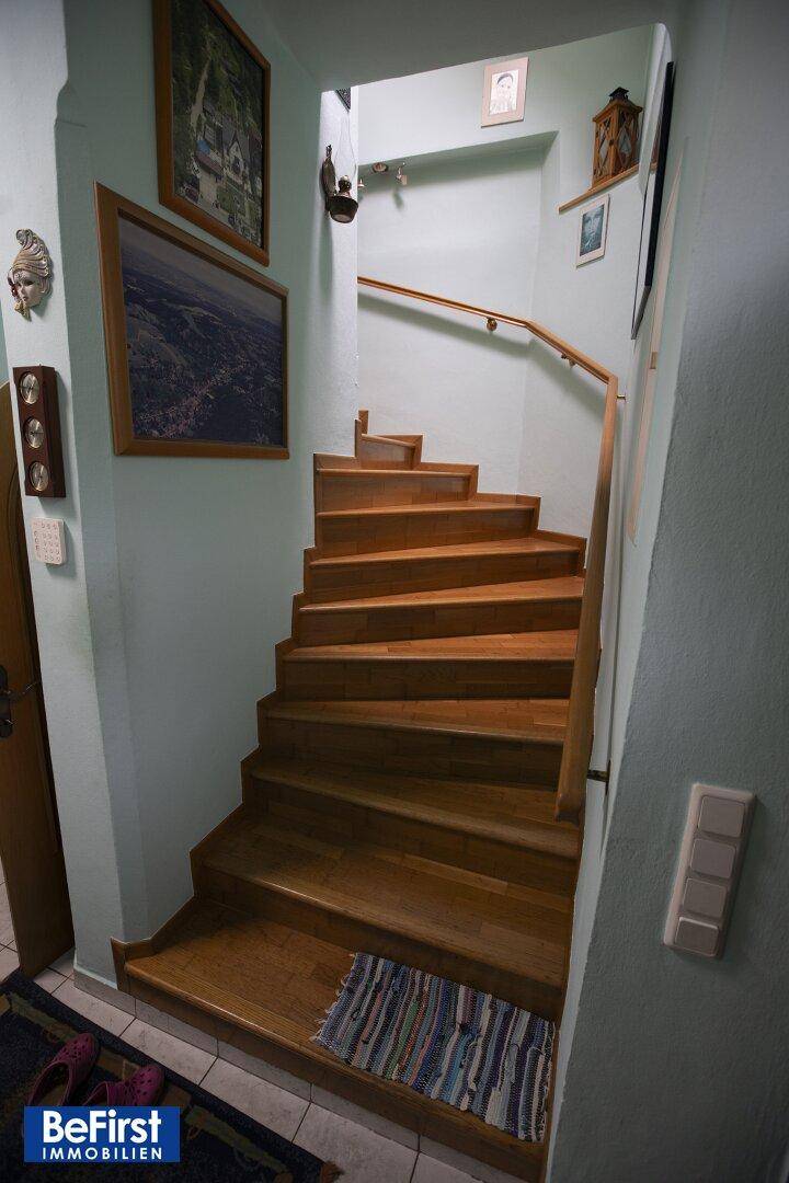 Helles Treppenhaus mit Holztreppe und Geländer, das die verschiedenen Etagen verbindet.