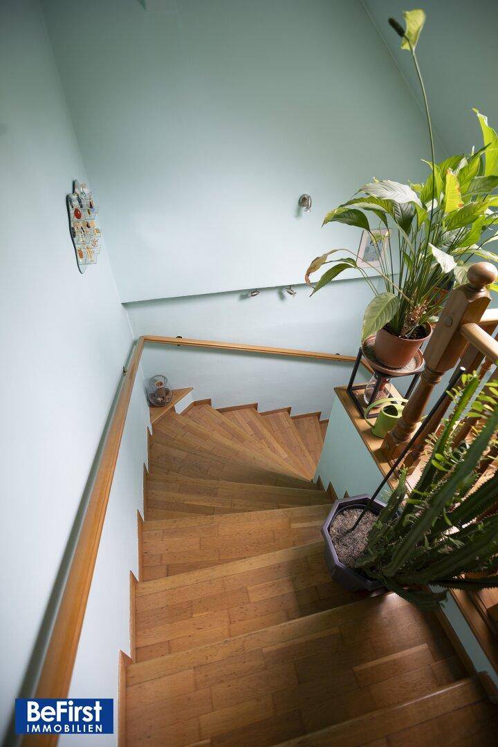 Holztreppe mit Geländer in einem hellen Treppenhaus, das die oberen Etagen erschließt.