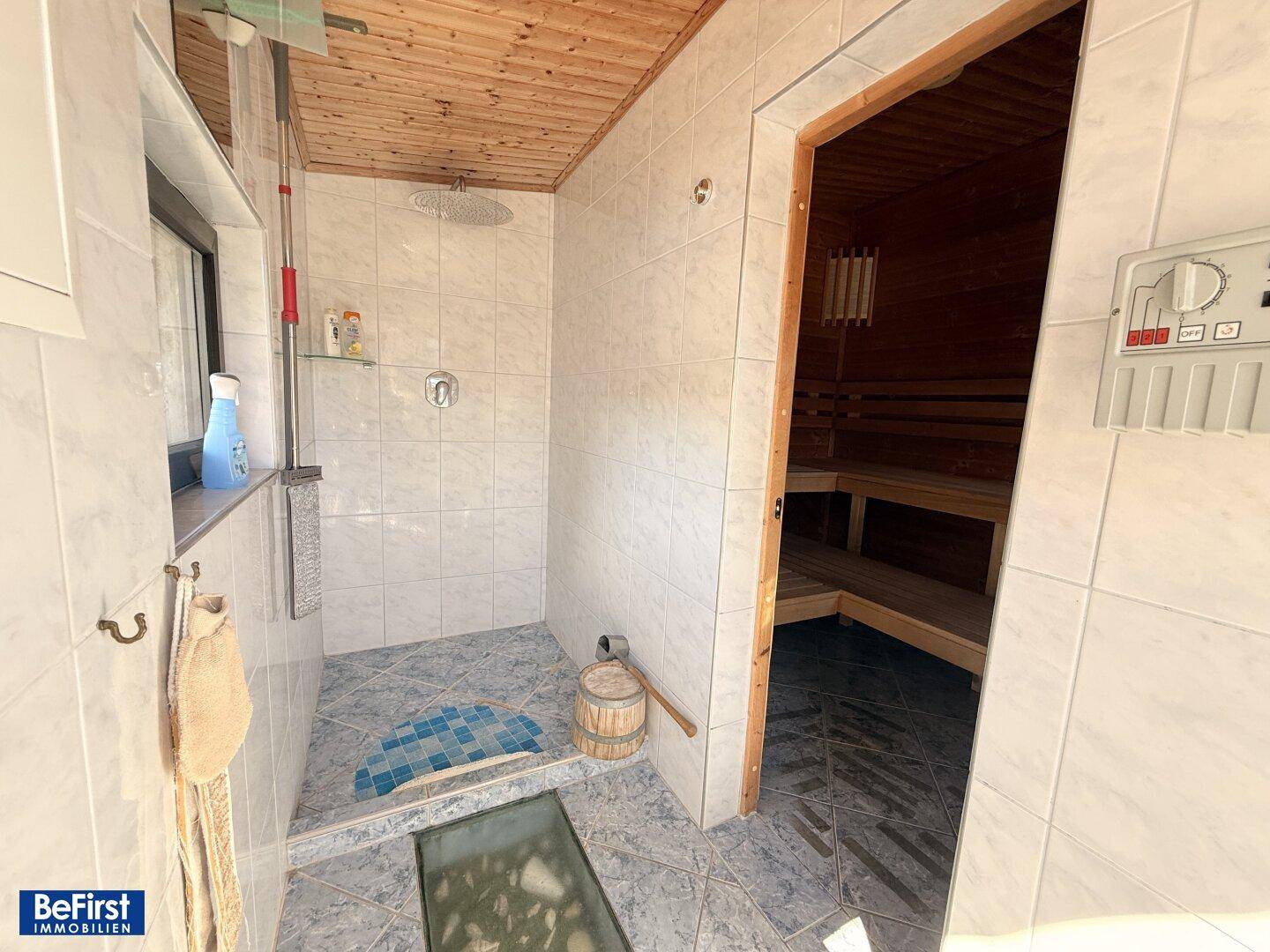 Modernes Badezimmer mit Duschbereich, hellen Fliesen und direktem Zugang zur Sauna.