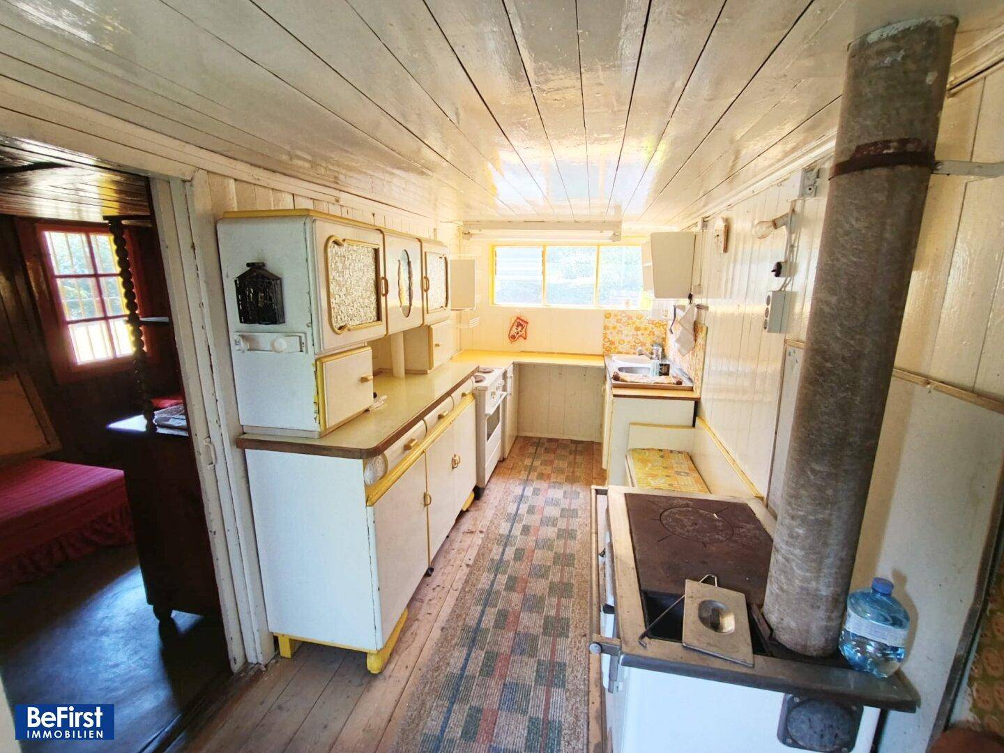 Kleine, rustikale Küche mit Holzofen, einfachen Schränken und Holzdecke.