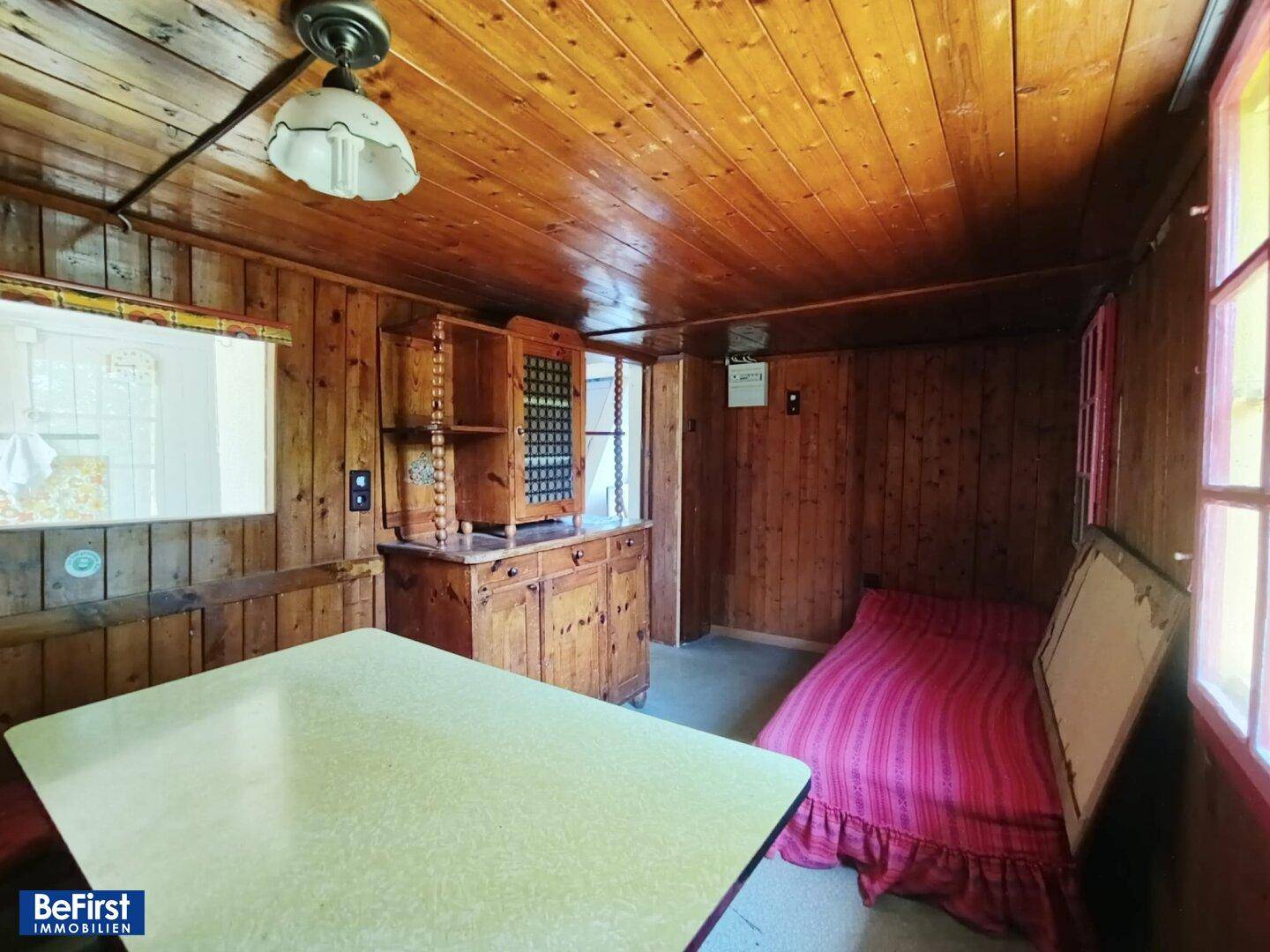Rustikaler Wohn- und Schlafbereich mit Holztäfelung, Tisch und einfachem Bett.
