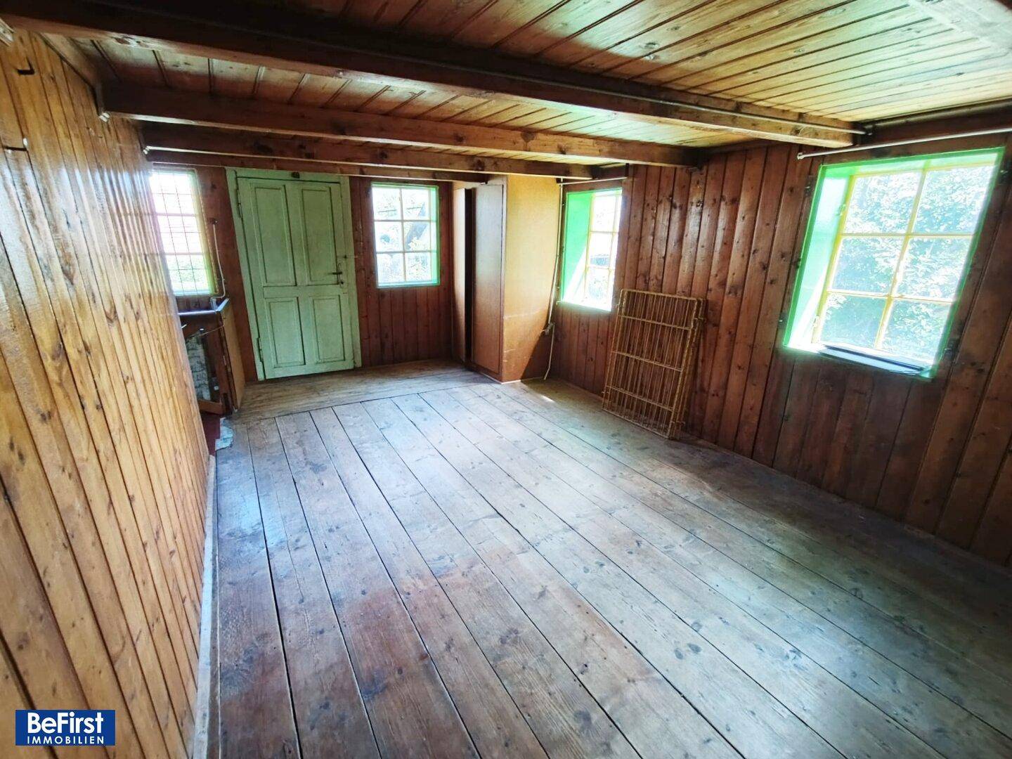 Geräumiges Zimmer mit Holzwänden, Holzboden und mehreren Fenstern für Tageslicht.