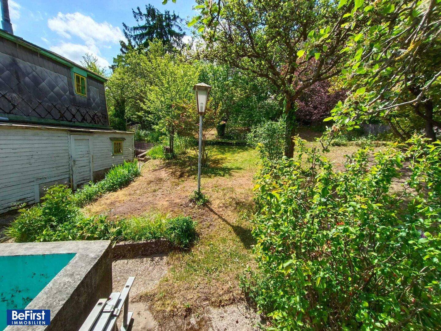Gartenansicht mit Laternenpfahl, üppigem Grün und Blick auf die Hausfassade.