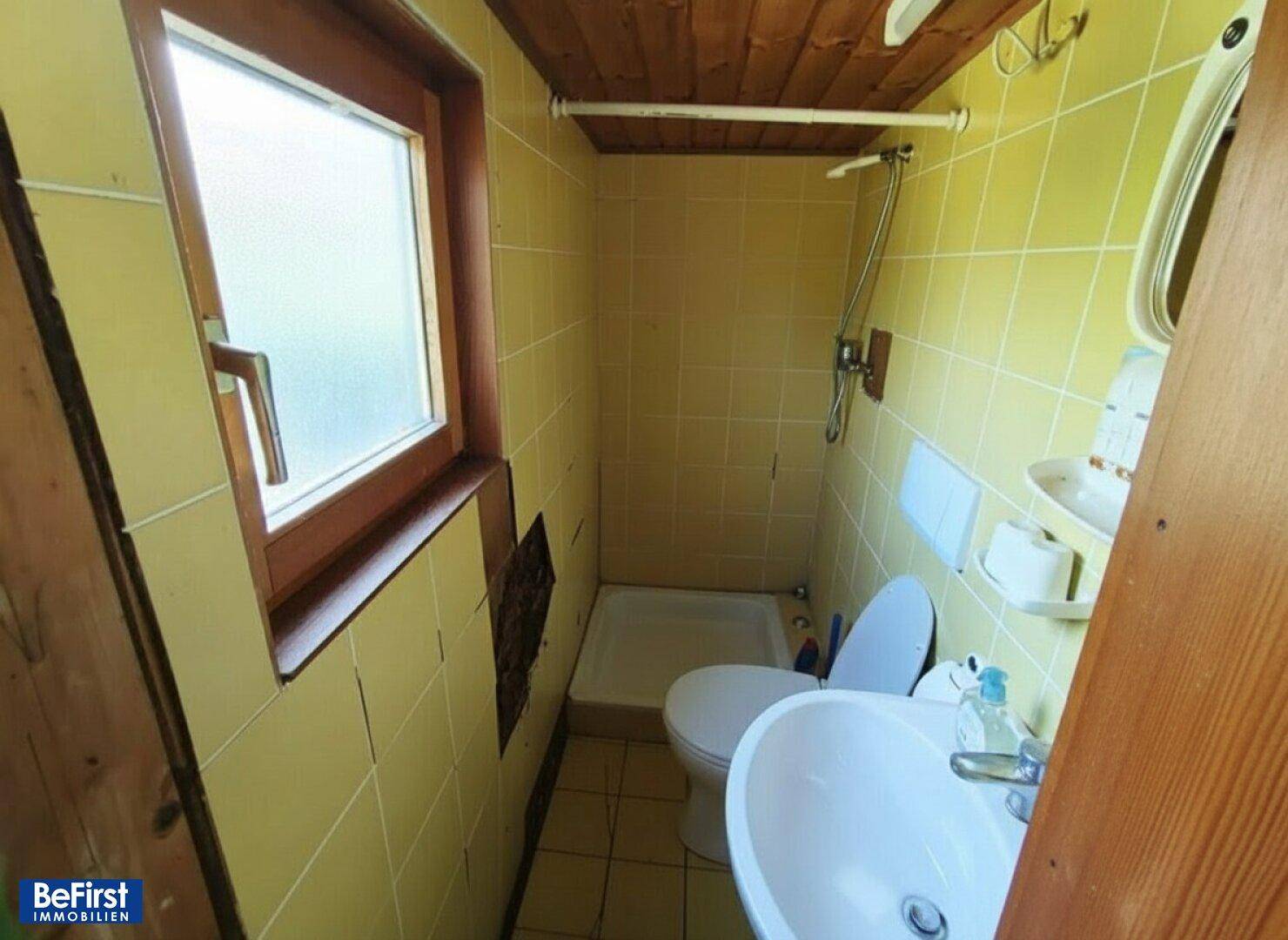 Kleines, einfaches Badezimmer mit gelben Fliesen, Dusche, WC und Fenster.