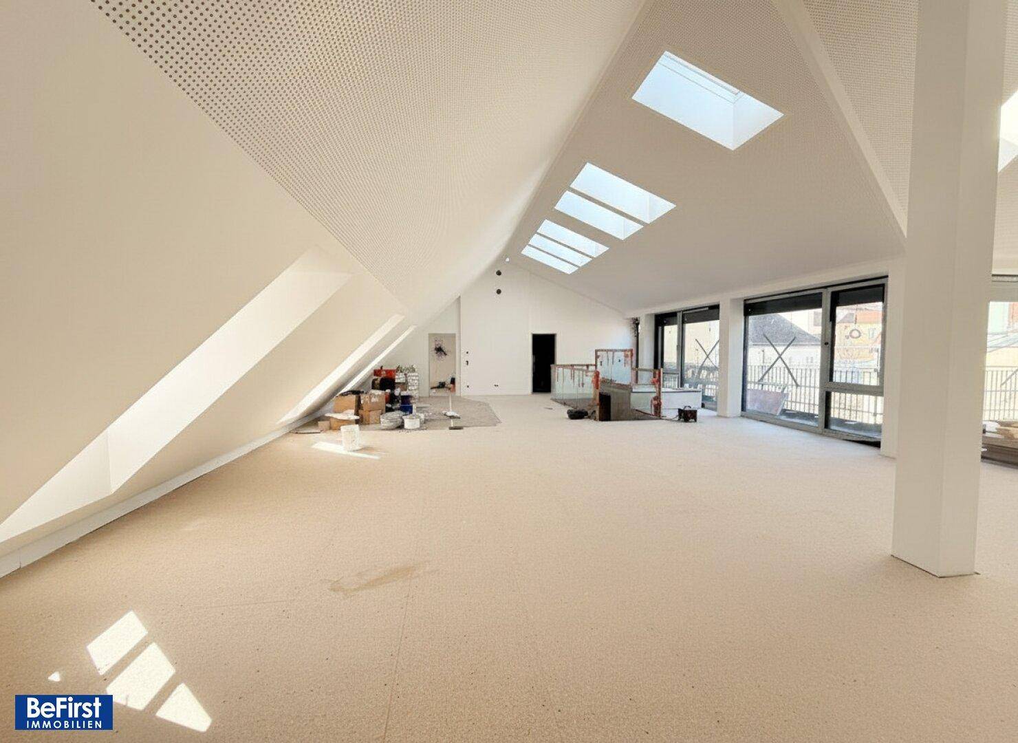 Weitläufiger Dachgeschoss-Loft mit schrägen Wänden, vielen Dachfenstern und Blick in den hinteren Bereich.