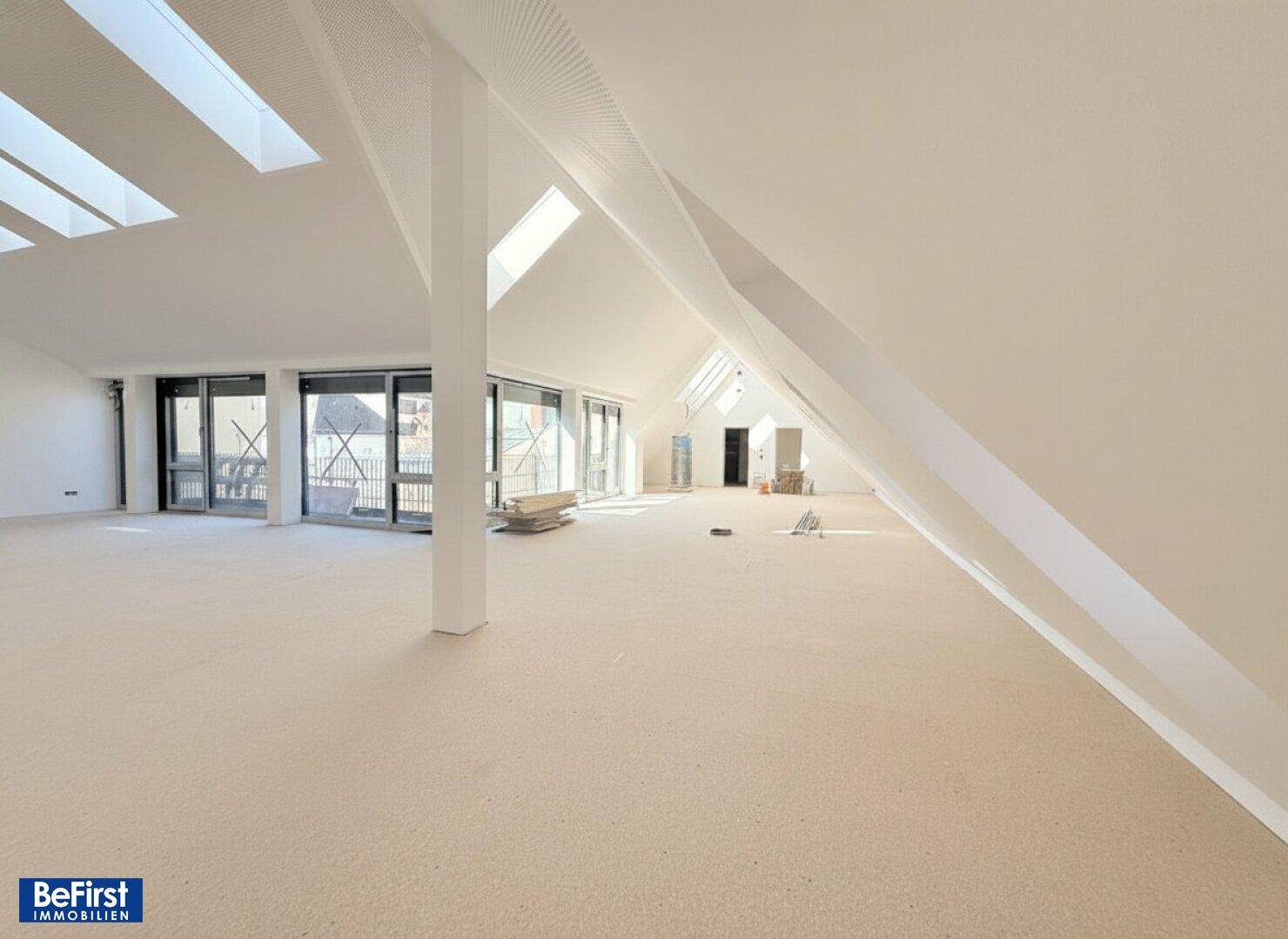 Großer, offener Dachgeschoss-Loft mit tragender Säule, schrägen Wänden und zahlreichen Dachfenstern.