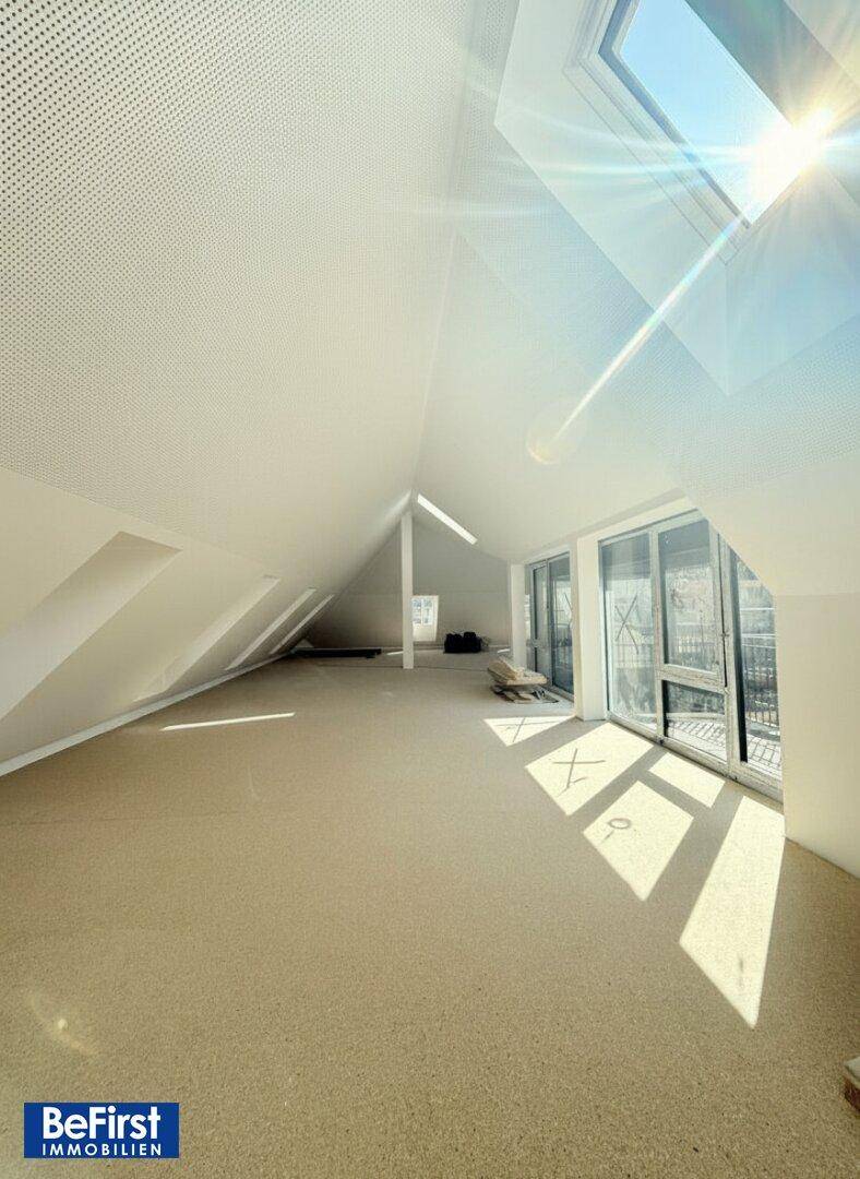 Heller Dachgeschoss-Loft mit schrägen Wänden und zahlreichen Dachfenstern, die viel Sonnenlicht hereinlassen.