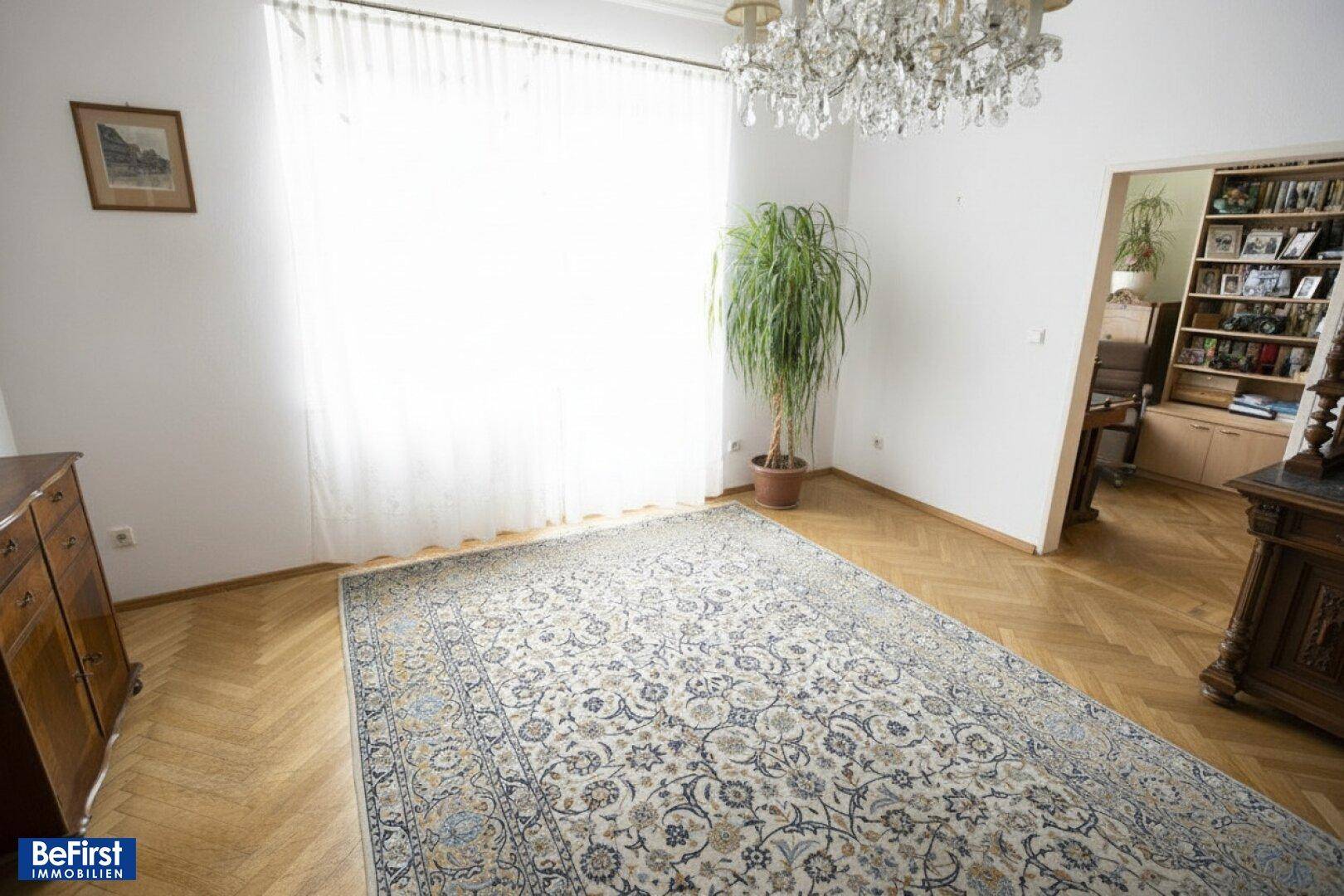 Elegantes Wohnzimmer mit Fischgrätparkett, großem Teppich und einem Kronleuchter an der Decke.