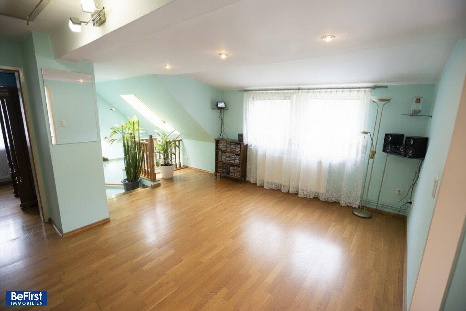 Helles Wohnzimmer im Dachgeschoss mit Holzfußboden, hellblauen Wänden und großen Fenstern.