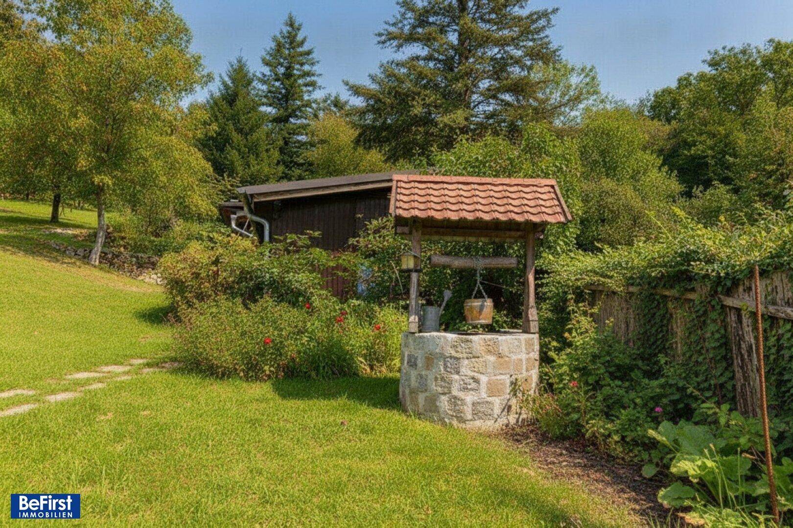 Ein idyllischer Gartenbereich mit einem traditionellen Brunnen und einem kleinen Gartenhaus im Hintergrund.