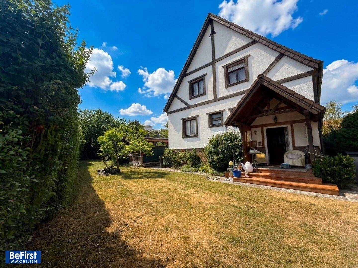 Seitlicher Blick auf das Haus mit Fachwerkdetails, einem gepflegten Garten und einer überdachten Terrasse.