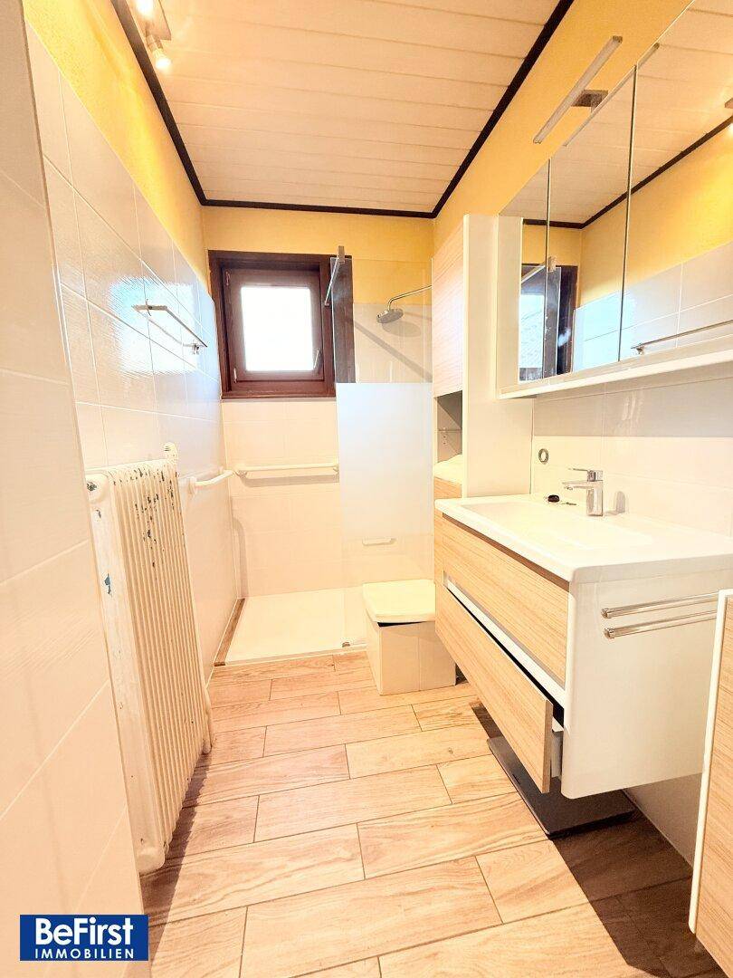 Modernisiertes Badezimmer mit Duschbereich, Waschtisch und Fenster.