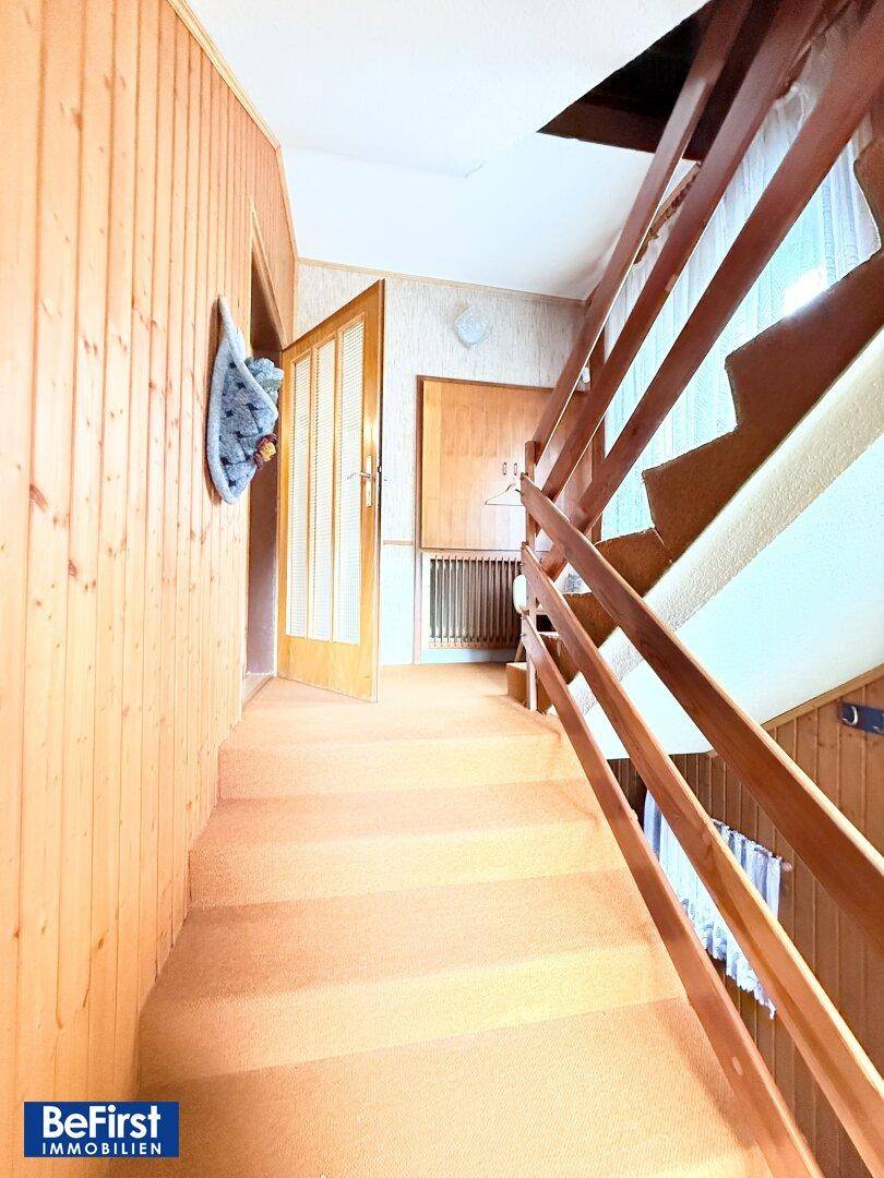 Holztreppe führt in das obere Stockwerk, umgeben von Holzvertäfelung.