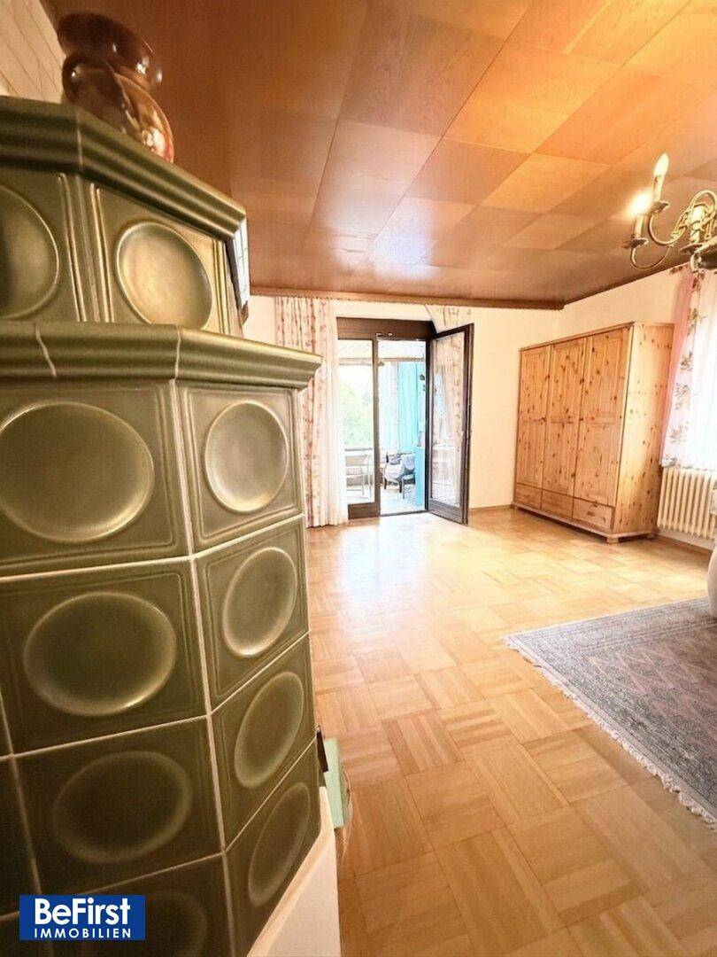 Wohnzimmer mit Kachelofen, Holzboden und Zugang zu einem Balkon oder einer Terrasse.