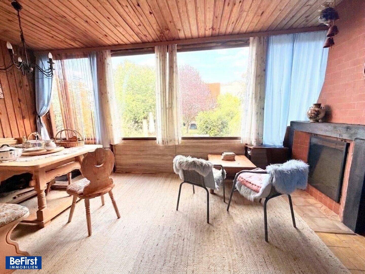 Gemütlicher Wohnbereich mit viel Holz, großen Fenstern und Blick ins Grüne.