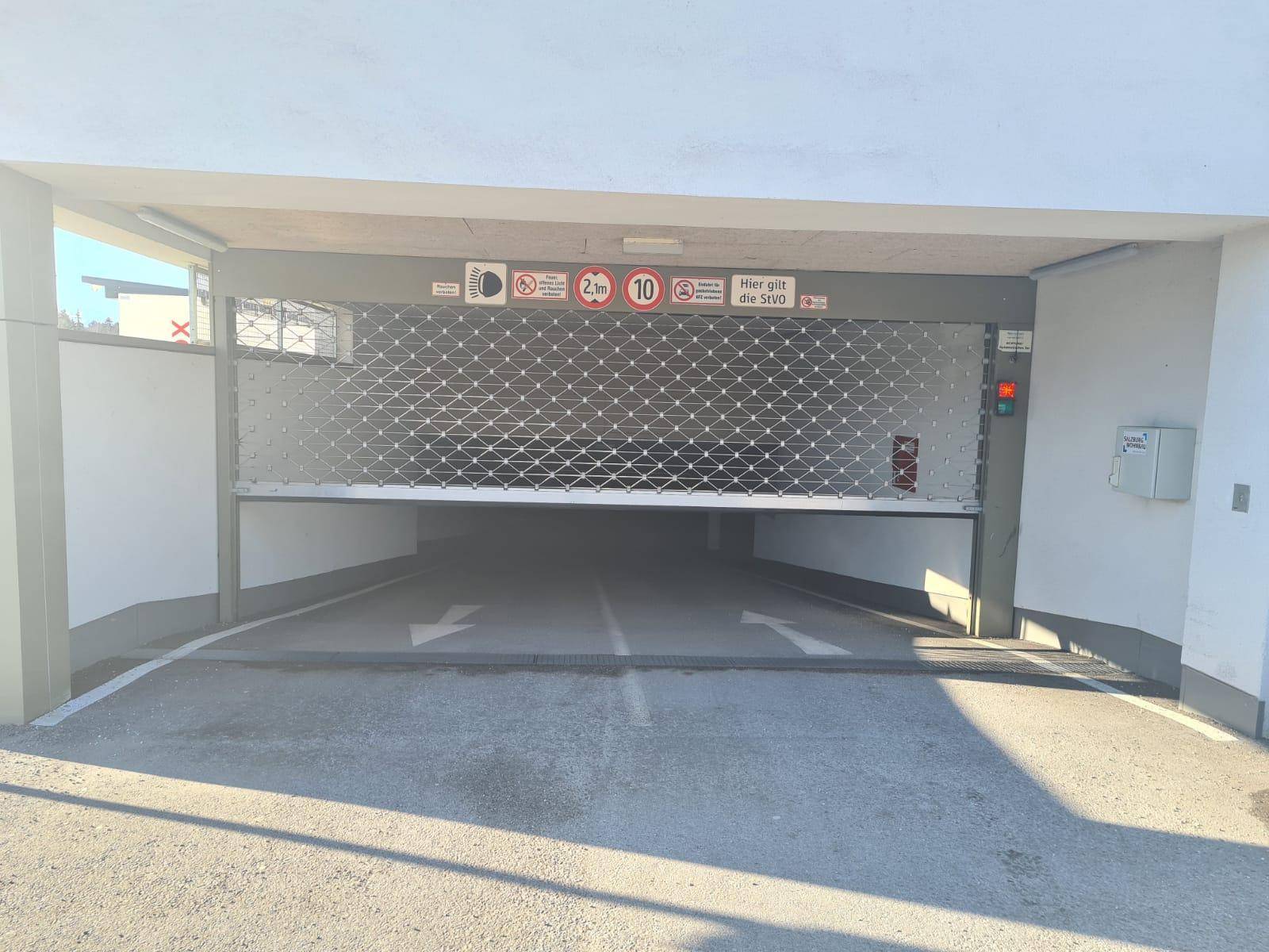Eingang zur Tiefgarage mit einem robusten Metallrolltor und Hinweisschildern.