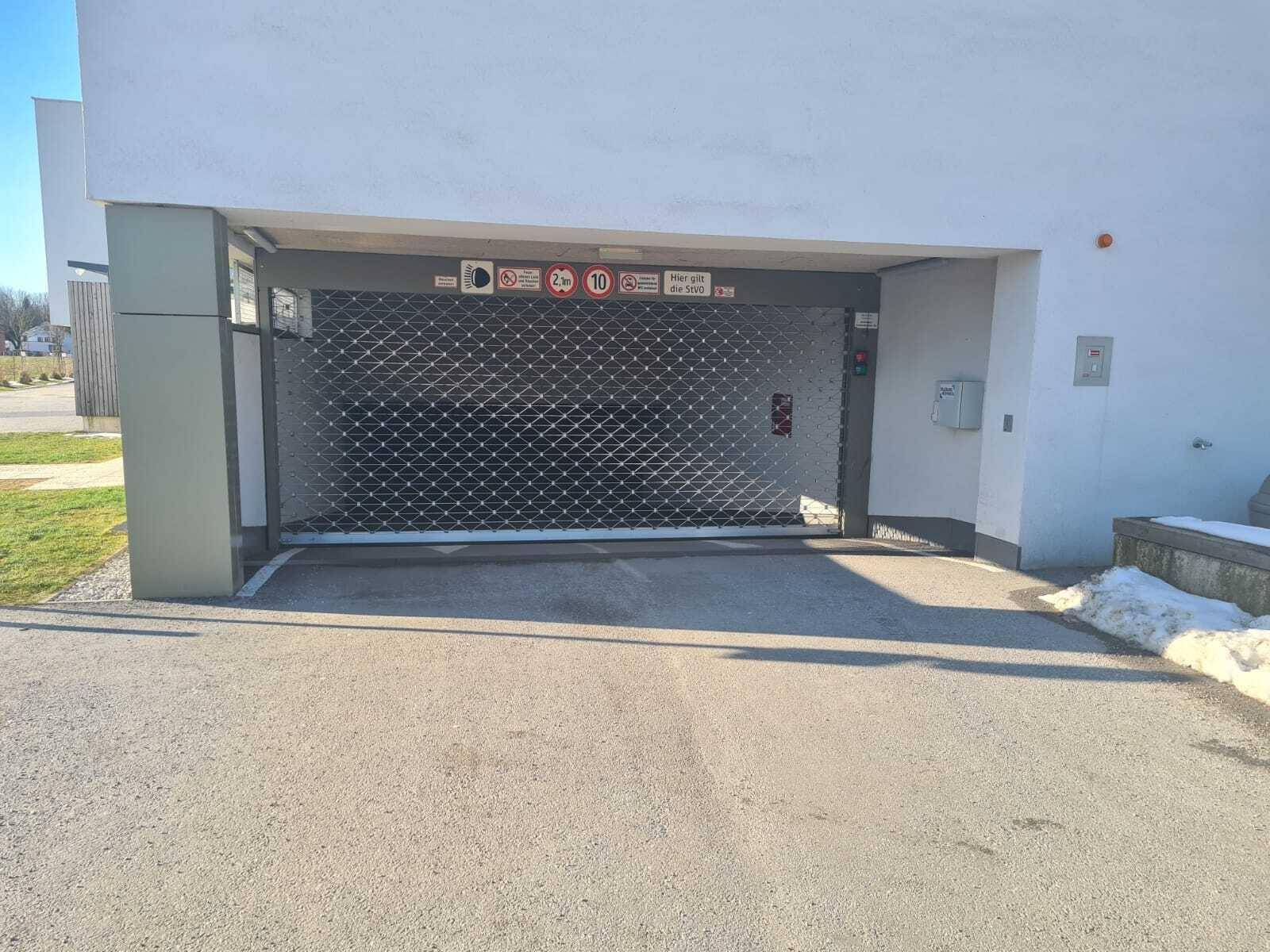 Außenansicht des Tiefgarageneingangs mit Rolltor und gepflegter Grünfläche im Vordergrund.